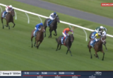 Jockeys in colorful silks race along a curved green turf track with a white rail, Racing.com live banner in corner.