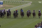 Horses and jockeys race down a grassy track with a curved white rail, spectators cheering on the right, timer overlay showing 1:21.99 (Hawkesbury R8).