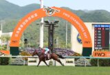 Horse and jockey racing past the finish line under an orange FWD champions arch with a digital scoreboard nearby and mountains in the background.