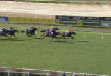 Horse race on a grassy racetrack with jockeys in colorful silks chasing the lead horse.