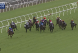 Group of jockeys on racing horses on a green turf track with white railings, timer reads 1:20.53.