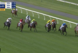 Horse race on a turf track with several horses and colorful jockey silks; timer shows 1:55.41 and a yellow '150m TO GO' banner, white railing along the course.