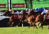 Horse race in progress with jockeys leaning forward; red Ladbrokes banners in the background.