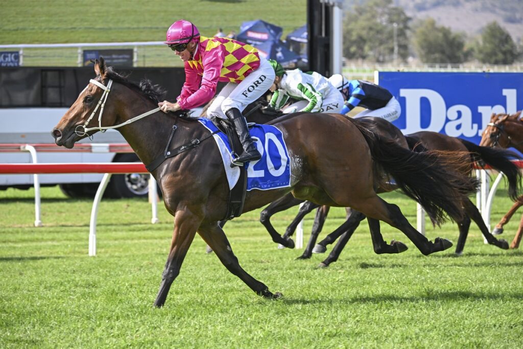 2301687.jpg | Just Horse Racing A jockey in pink and yellow silks rides a brown racehorse wearing number 20, leading a sprint on a grassy track.