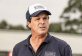 Man in a navy polo and light cap standing outdoors, looking to the right.