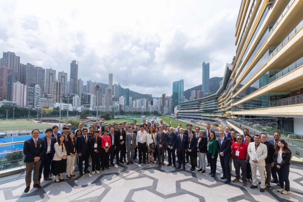 Group of professionals in business attire posing for a photo on a rooftop terrace with a city skyline and a curved modern building on the right.