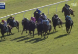 Horse race on a grassy track, jockeys in colorful silks sprinting toward the bend with a timer overlay 0:59.91 on screen to the left.