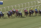 A crowded horse race on a green turf track with colorful jockey silks riding side by side along the inner rail; timer shows 0:50.17.