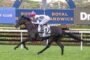 Jockey in pink cap rides a black horse jumping at a racecourse with Royal Randwick signage behind them in mid-air.
