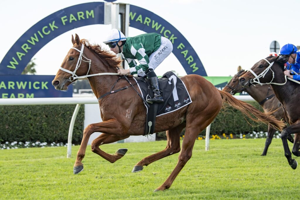 Horse and jockey in green-and-white silks sprint toward the finish at Warwick Farm racecourse, with a blue-green arch behind them.