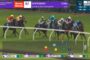Group of galloping horses on a green turf racecourse with jockeys in colorful silks; on-screen graphics show race info and current placings/odds.