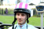 Young man wearing a pink-striped helmet with LAS logo, outdoors and smiling slightly.