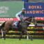 Horse and rider in mid-gallop on a racecourse with colorful sponsor banners in the background, including 'Sporting Chance Cancer Foundation' and 'Royal Randwick' signage.