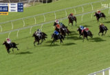 Thoroughbred horse race on a grassy track with colorful jockey silks close to the inside rail; 120m to go countdown on screen.