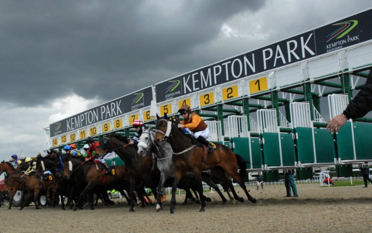 Horses and jockeys burst from the starting stalls at Kempton Park racecourse under dark clouds. ','Group of horse racers at the Kempton Park starting line, riders leaning forward as they speed off. ','Starting gates at Kempton Park with yellow numbered panels and jockeys on sprinting horses. ','Jockeys in colorful silks race from the gates at Kempton Park while a spectator stands nearby. ','Overhead view of a horse race launch at Kempton Park with a cloudy sky.