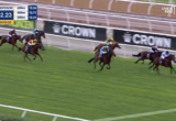 Horse race at Flemington, several jockeys ride galloping horses on a green turf with a timer showing 2:32.23 and 120m to go.