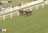 Two horses neck-and-neck on a green turf track with white rails; jockeys in blue and orange; spectators in the background; live broadcast overlay visible (Royal Ascot). Description of race action and setting only, no extraneous details.