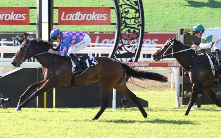 Two jockeys race side by side on galloping horses with Ladbrokes banners in the arena.