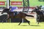 Two jockeys race side by side on galloping horses with Ladbrokes banners in the arena.