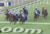 Horse race in progress with jockeys on a curved track; scoreboard shows 2:15.13 and 280m to go, camera on leading pack.