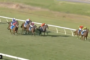 Group of jockeys riding horses in a race on a grassy track, turning a bend, with colorful silks.