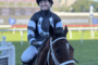Jockey in blue-and-black racing silks smiles while riding a dark brown horse on a race track.