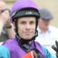 Close-up of a person wearing a purple helmet and purple-teal racing suit, looking at the camera with a neutral expression.